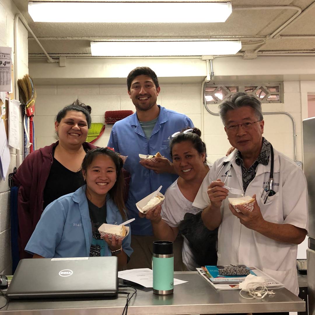 Five clinic staff holding small containers of food, while gathered around a desk.